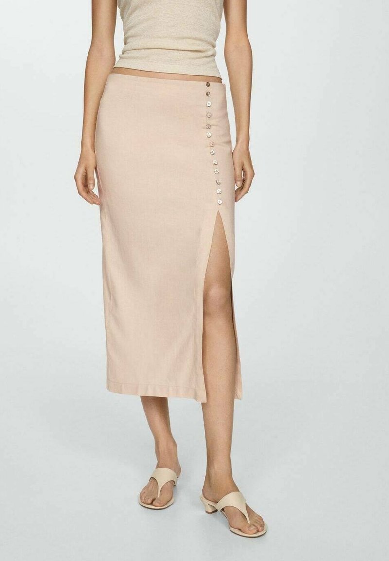 Femme portant une jupe midi beige avec une fente latérale et des boutons décoratifs, associée à des sandales beiges à talons et un haut sans manches.