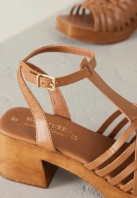 Tan leren blockhakken sandalen met een strap-design. Voorzien van een verstelbare enkelband met een gouden gesp en een houten hak.