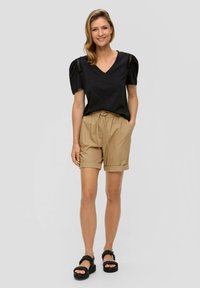 Czarny top z dekoltem w serek, z bufiastymi rękawami i koronkowymi detalami, w połączeniu z beżowymi szortami z elastycznym pasem i podwiniętymi mankietami, uzupełniony czarnymi sandałami.