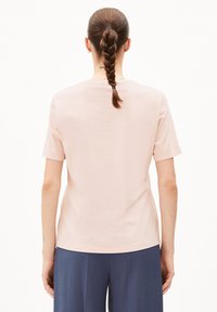 Lichtroze t-shirt met korte mouwen en een ronde hals, gemaakt van een gladde stof en in een relaxte pasvorm, gecombineerd met donkerblauwe broek met wijde pijpen.