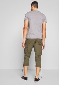 Graues Kurzarm-T-Shirt, olivgrüne Cargo-Hose mit Seitentaschen und schwarze Sneakers mit weißen Akzenten. Die Hose hat verstellbare Bänder am Saum.