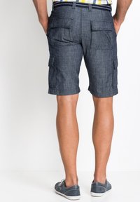 Pantaloni cargo in lino blu scuro, con molteplici tasche, dettagli cuciti e fronte piatto. Indossati con scarpe casual.