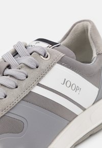 Gros plan sur des baskets JOOP! grises et blanches avec des lacets texturés, des accents en daim et un col rembourré sur fond blanc.