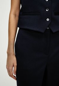 Nauwsluitend marineblauw vest en broek met verticale ribbelstructuur, voorzien van een zesknopensluiting aan de voorkant en zijzakken.