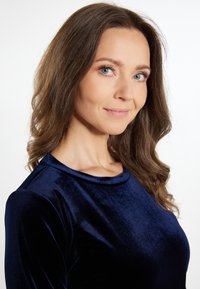 Sötétkék bársony felső kerek nyakkivágással és hosszú ujjakkal, sima textúrával és testre simuló fazonnal, amely kiemeli a dekoltázst.