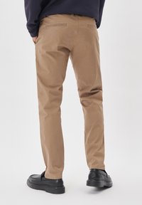 Beige bombažne chinos hlače s ravnim krojem, ki imajo dve zadnji žep in gladko teksturo. V kombinaciji s črnimi natikači.