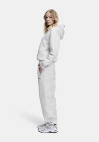 Grå huvtröja och joggers i mjuk fleece, med en känguruficka och broderad detalj. Kombinationen är kompletterad med vita sneakers.