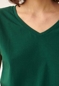 Maglietta verde a V in cotone morbido, con una texture liscia. Il collo è cucito in modo pulito con una leggera lucentezza.