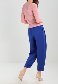 Ljust rosa stickad tröja med strukturerat mönster och långa ärmar, kombinerad med löst sittande kungligt blå byxor och nudefärgade klackar.