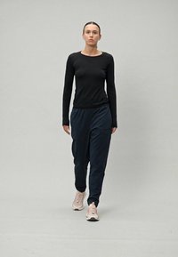 Svart langermet topp kombinert med marineblå joggebukser og lyse rosa joggesko. Glatt stoff, avslappet passform og minimalistisk design uten synlige mønstre.