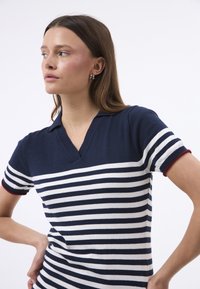 Tumesinine triibuline polo-särk valgete horisontaalsete triipudega ja punaste aktsentidega varrukatel. Pehme kangas klassikalise V-kaelusega disainiga.