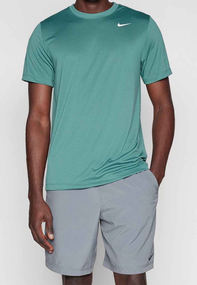 T-shirt de sport vert à manches courtes en tissu léger, assorti à un short gris clair. Présente le logo Nike sur le t-shirt.