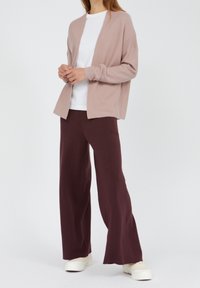 Jasnoróżowy kardigan z otwartym przodem na białej koszulce, w połączeniu z luźnymi, bordowymi spodniami i białymi trampkami. Miękka tekstura, luźny krój.