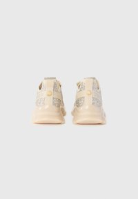 Zapatillas beige con acentos de strass, suelas gruesas y lengüetas de tela, mostradas desde atrás sobre un fondo blanco liso.