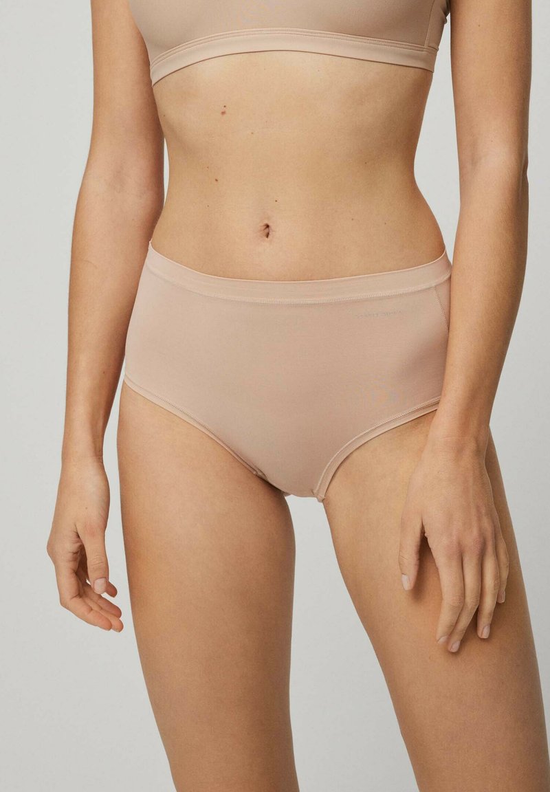 Ropa interior de talle alto beige con una tela suave y elástica. Presenta un diseño sin costuras y un logo sutil cerca de la cintura.