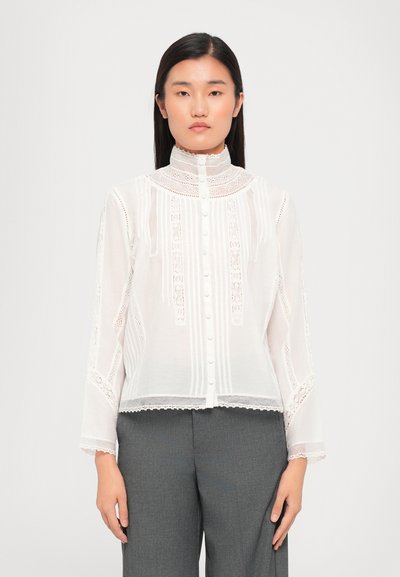 Blouse blanche transparente avec un délicat détail en dentelle, des rayures verticales et un col haut, avec des boutons sur le devant.