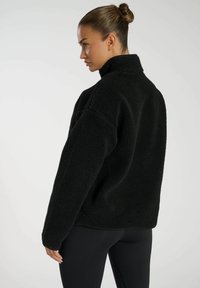 Giacca pullover in pile nera con colletto alto, vestibilità over size e superficie testurizzata, con maniche lunghe e orlo dritto in vita.