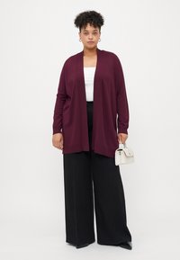 Burgundy cardigan with an open front, long sleeves, and lightweight knit fabric. Paired with black wide-leg pants and a small white handbag.