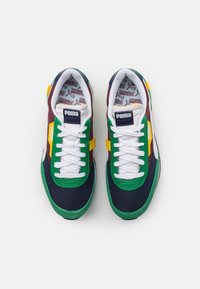 Chaussures de sport présentant un design multicolore avec des panneaux bleu marine, vert, jaune et bordeaux, des lacets blancs et des semelles en caoutchouc texturées.