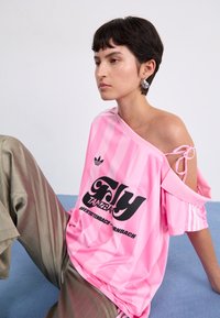 Rosa randig oversized t-shirt med svart grafisk text, med off-the-shoulder design och knytaccent, kombinerat med grå randiga byxor.