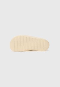 Sula av en sko, med ett slätt, ljust beige gummimaterial och ett strukturerat rutmönster för grepp. Rund tå och platt design.