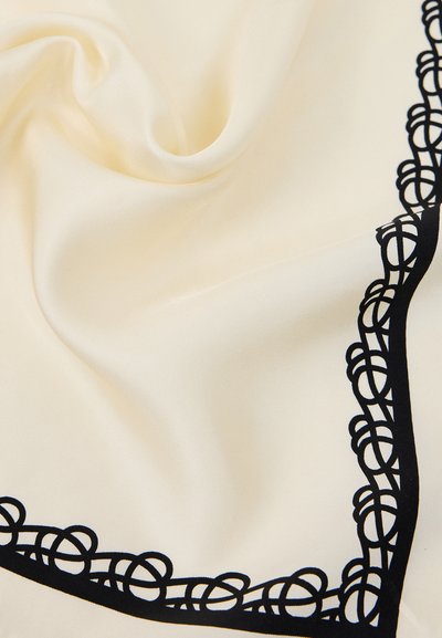Tissu couleur crème avec une bordure décorative noire présentant des boucles entrelacées le long du bord.