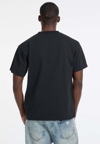 T-shirt en coton noir avec un col rond et des manches courtes, vue de dos, associée à un jean en denim bleu clair déchiré.