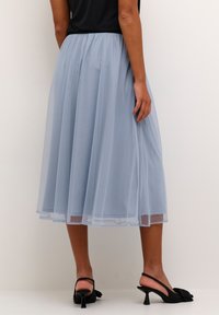 Világoskék, térd hosszúságú tüll szoknya ráncolt derékkal. Fekete, csatos magassarkú cipővel kombinálva, amelyen masni díszítés található. Sima textúra.