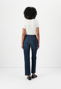 Hvit kortermet T-skjorte med rund hals, kombinert med mørkeblå rett-buks jeans med baklommer og et svart belte.
