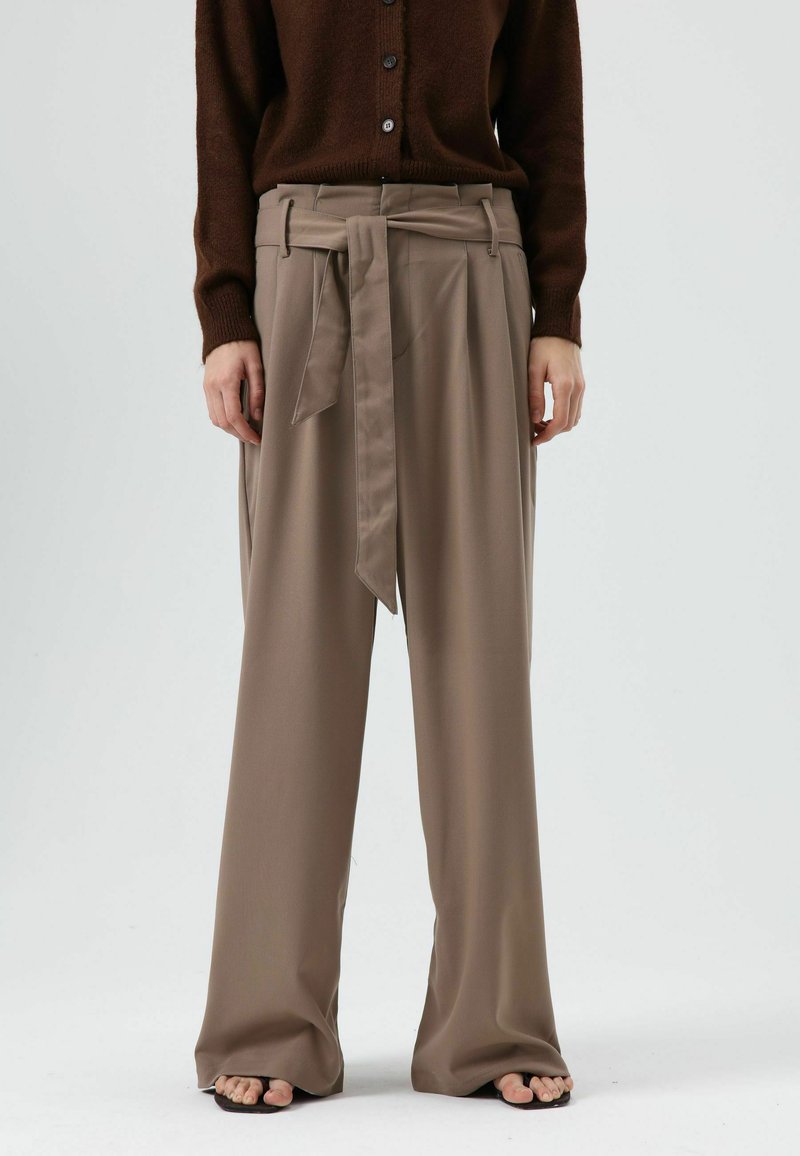 Broek met hoge taille van een zachte, lichtbruine stof met een wijde pijp en een ceintuur die gestrikt kan worden, afgewerkt met plooien aan de voorkant voor extra textuur.