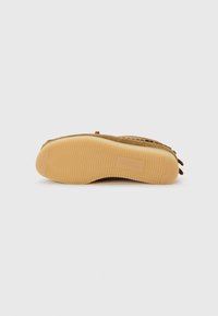 Chaussure en suède marron avec une semelle en caoutchouc. La semelle a une surface texturée et arbore un logo. La chaussure a une forme arrondie et des bords doux.