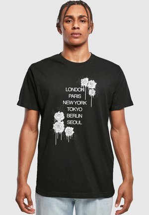 Sort bomulds t-shirt med hvide rosedesigns og bynavne: London, Paris, New York, Tokyo, Berlin, Seoul, trykt i lodret orden.