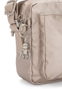 Beige nylon bag with a zip closure, featuring a textured surface and a metal monkey charm attached to the zipper.