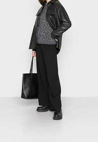 Černá kožená oversize košile, vzorovaný černobílý top, černé široké kalhoty a masivní černé kotníkové boty. Nese strukturovanou černou tašku.