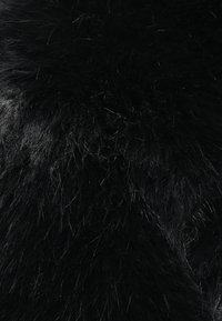 Μαύρη συνθετική γούνα με μακριές, πυκνές ίνες. Η υφή φαίνεται απαλή και πλούσια, με διακριτικές μεταβολές στη γυαλάδα και την αντανάκλαση του φωτός.