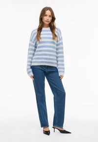 Suéter esponjoso con rayas azules y blancas y cuello redondo, combinado con jeans azul de pierna recta y tacones negros de punta afilada.