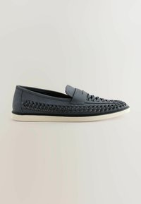 Mocasines azul oscuro hechos de cuero suave, con detalles trenzados y una suela de goma blanca. Diseño de perfil bajo con una correa acolchada en el empeine.