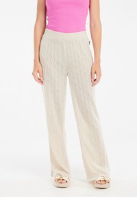 Beige, lichte, gebreide broeken met ruitpatronen, wijde pijpen en een elastische tailleband, gecombineerd met een roze zonder mouwen top.