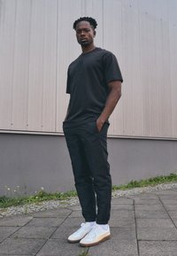 Svart bomullströja med korta ärmar, med en liten design på bröstet, tillsammans med smala svarta byxor och vita sneakers.