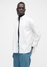 Valge triibuline nööpidega pikkade varrukatega särk, kantud musta kõrge kaelusega pluusi peal, sobitatud hele siniste teksadega. Lihtne ja vabaaja stiil.