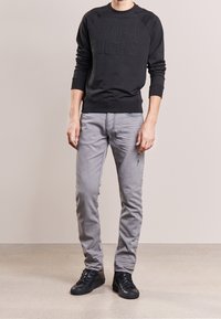 Black crewneck sweatshirt with embossed "ARMANI JEANS" logo, paired with light grey slim-fit jeans and black lace-up sneakers.