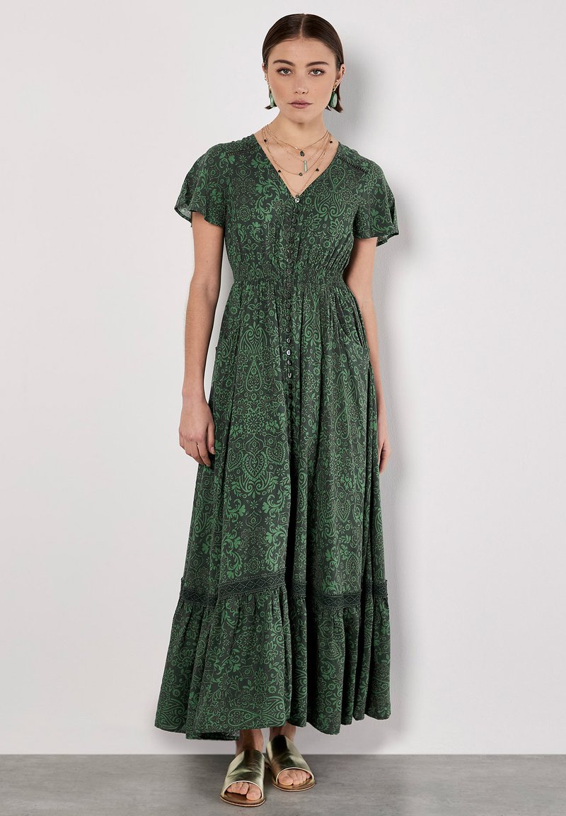 Groene maxi-jurk met een patroon, korte mouwen, V-hals, elastische taille en een gelaagde rok. Gepaarde met gouden sandalen.