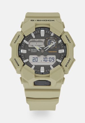 Orologio G-SHOCK con cinturino in resina khaki, display digitale e analogico, quadrante nero, indicatori bianchi in contrasto e diversi pulsanti funzione.