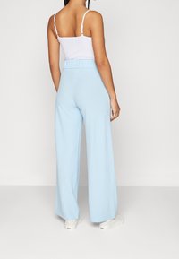 Lichtblauwe wijde broek gemaakt van zachte stof, met een elastische tailleband in een relaxte pasvorm, gecombineerd met een witte camisole.