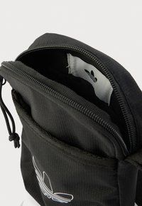 Črna tkaninska torba z zadrgo, na kateri je bel logotip znotraj. Zunanjost ima teksturiran vzorec in vrvico za zapiranje.