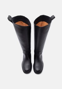 Μαύρες δερμάτινες μπότες μέχρι το γόνατο με λείο εξωτερικό, στρογγυλή μύτη και μπεζ επένδυση. Διαθέτουν θηλιές για εύκολο φόρεμα.