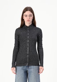 Langermet svart ribbestrikket topp med metallisk tråd, høy krage og knappdetalj foran. Iført med lyseblå vide jeans.