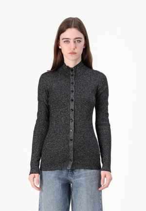 Long-sleeve black ribbed top with metallic threading, high collar, and button front detail. Worn with light blue wide-leg jeans.