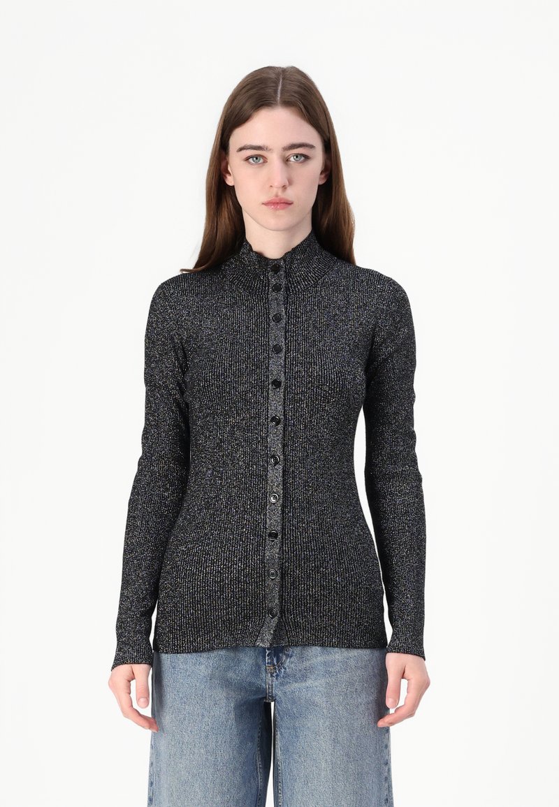 Langermet svart ribbestrikket topp med metallisk tråd, høy krage og knappdetalj foran. Iført med lyseblå vide jeans.