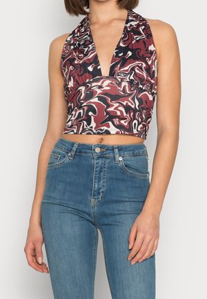Frau trägt ein ärmelloses, bordeauxrotes, schwarzes und weißes abstraktes bedrucktes Neckholder-Crop-Top mit tiefem V-Ausschnitt und hoch taillierte blaue Jeans.